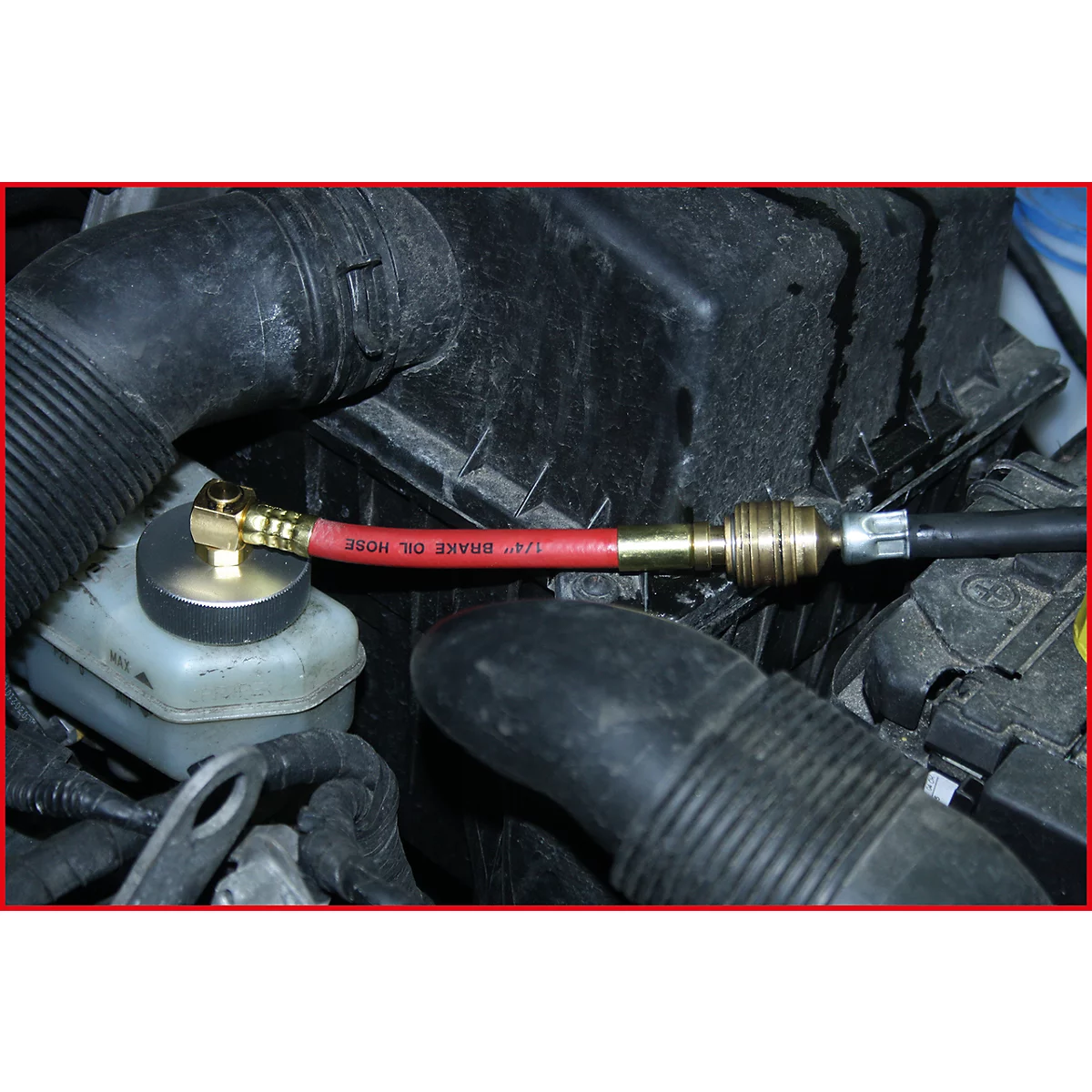 Nahaufnahme eines roten Bremsschlauchs mit Schriftzug und Metallverbindungen im Motorraum.